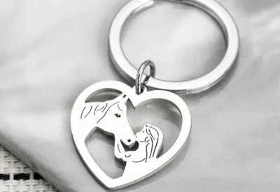Ein Schlüsselanhänger „Herz mit Pferd und Mädchen“ mit einem eingravierten Pferd und einem Fohlen, die auf einer strukturierten weißen Oberfläche ruhen.